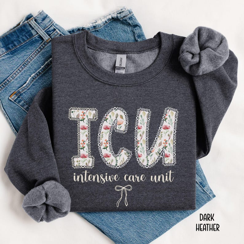 A "Dark Heather" sweatshirt, featuring the letters "ICU" in a block font filled with a green, pink, and white floral pattern with a decorative border, and the words "intensive care unit" and a bow below.