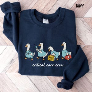 A "Navy" sweatshirt, featuring four cartoon geese dressed as an ICU medical team, with the text "critical care crew" printed below.