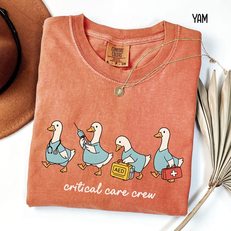 A "Yam" Comfort Colors t-shirt featuring four cartoon geese dressed as an ICU medical team, with the text "critical care crew" printed below.