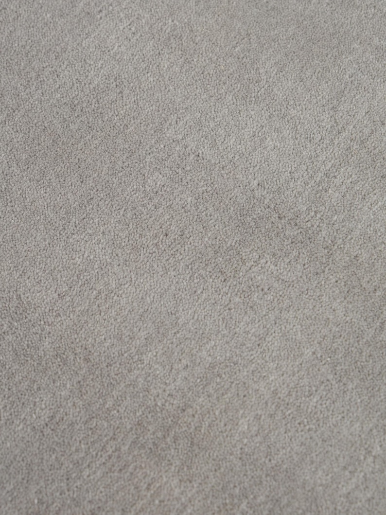 May include: Close-up of a light gray, textured fabric. The surface has a slightly uneven appearance, with a subtle, speckled pattern. The fabric appears soft and could be used for upholstery or clothing.