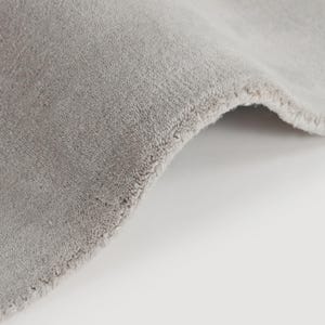 May include: Close-up of a section of a light gray rug with a soft, textured surface. The edge of the rug is visible, showing a neatly finished border. The rug is folded over, revealing its thickness and construction.