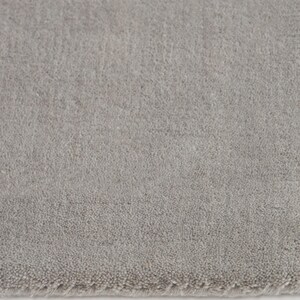 May include: A close-up of a light gray rug with a soft, textured surface. The rug has a subtle, uniform color and a slightly blurred edge, suggesting a plush, comfortable texture. The neutral tone makes it suitable for various interior design styles.