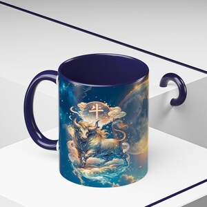 Puede incluir: Taza de cerámica con interior y asa azul oscuro. El exterior presenta una ilustración detallada de un toro, nubes y elementos celestiales. El diseño incluye caracteres chinos. La taza está sobre un fondo blanco.