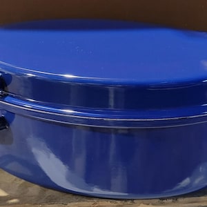 May include: A cobalt blue oval-shaped enamel roasting pan with a matching lid. The pan has two curved handles on each side. The lid fits snugly on top, creating a complete and functional cooking vessel. The glossy finish reflects light.
