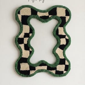 Hand tufted checkerboard mirror frame with a forest green border hanging on a plain off-white wall.