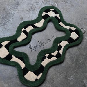 Pu&ograve; includere: Un tappeto dalla forma irregolare e ondulata con un bordo spesso verde scuro e un motivo a scacchi neri e crema. Il centro &egrave; aperto e il testo Rugs By Avnoor &egrave; stampato al centro. Due anelli in metallo argentato sono fissati nella parte superiore.