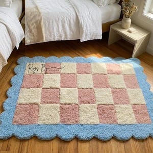 Pink checkerboard scalloped handmade wool rug styled beside a bed in a bright bedroom.
