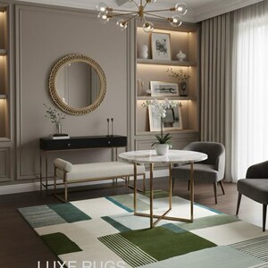 May include: A modern living room with a geometric patterned rug. The rug features green, blue, and white rectangles. A round marble table and two gray chairs are in the center. A gold chandelier hangs above. The text "LUXE RUGS" is visible.