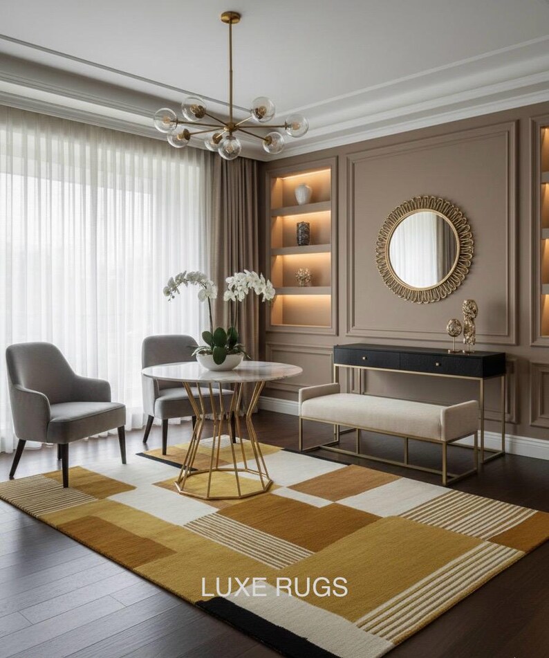 May include: A modern living room featuring a geometric patterned rug in shades of gold, white, and black. The room includes a round marble table, two gray chairs, a bench, and a decorative mirror. A chandelier hangs above the table. The text "LUXE RUGS" is visible.