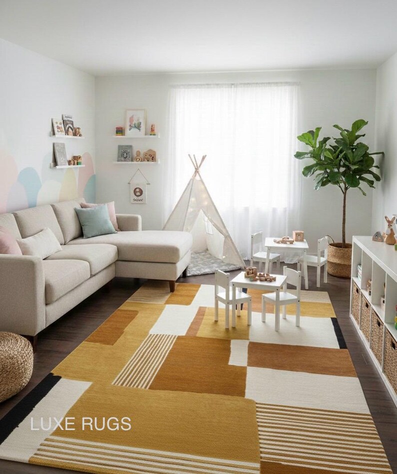May include: A modern living room with a beige sectional sofa, white tables and chairs, and a geometric rug in shades of yellow, brown, and white. A teepee and a potted plant add to the room's decor. The rug has the text "LUXE RUGS".