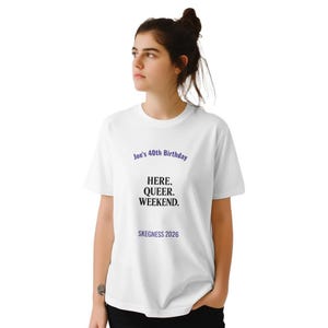May include: White t-shirt featuring the text "Joe's 40th Birthday" in purple, with "HERE. QUEER. WEEKEND." in black, and "SKEGNESS 2026" in blue. The shirt is being worn by a person.