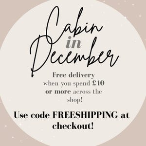 May include: A promotional graphic with the words "Cabin in December" in elegant script. The text is set against a soft beige background with subtle star accents. Additional text promotes free delivery.