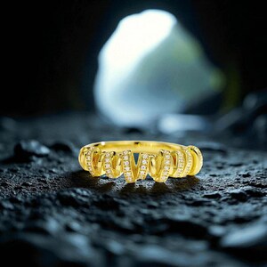 May include: A gold ring featuring a spiral design, adorned with small diamonds. The ring is set on a dark, textured surface, with a blurred, bright background.