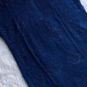 May include: A navy blue tunic top with intricate embroidered detailing. The top features a round neckline with a small slit and short sleeves. The fabric appears lightweight and is displayed on a wooden hanger.