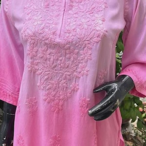 Puede incluir: Una t&uacute;nica rosa con bordados florales. La parte superior presenta un cuello redondo, mangas tres cuartos y un efecto de color degradado de rosa claro a oscuro. El bordado se concentra en el &aacute;rea del pecho.