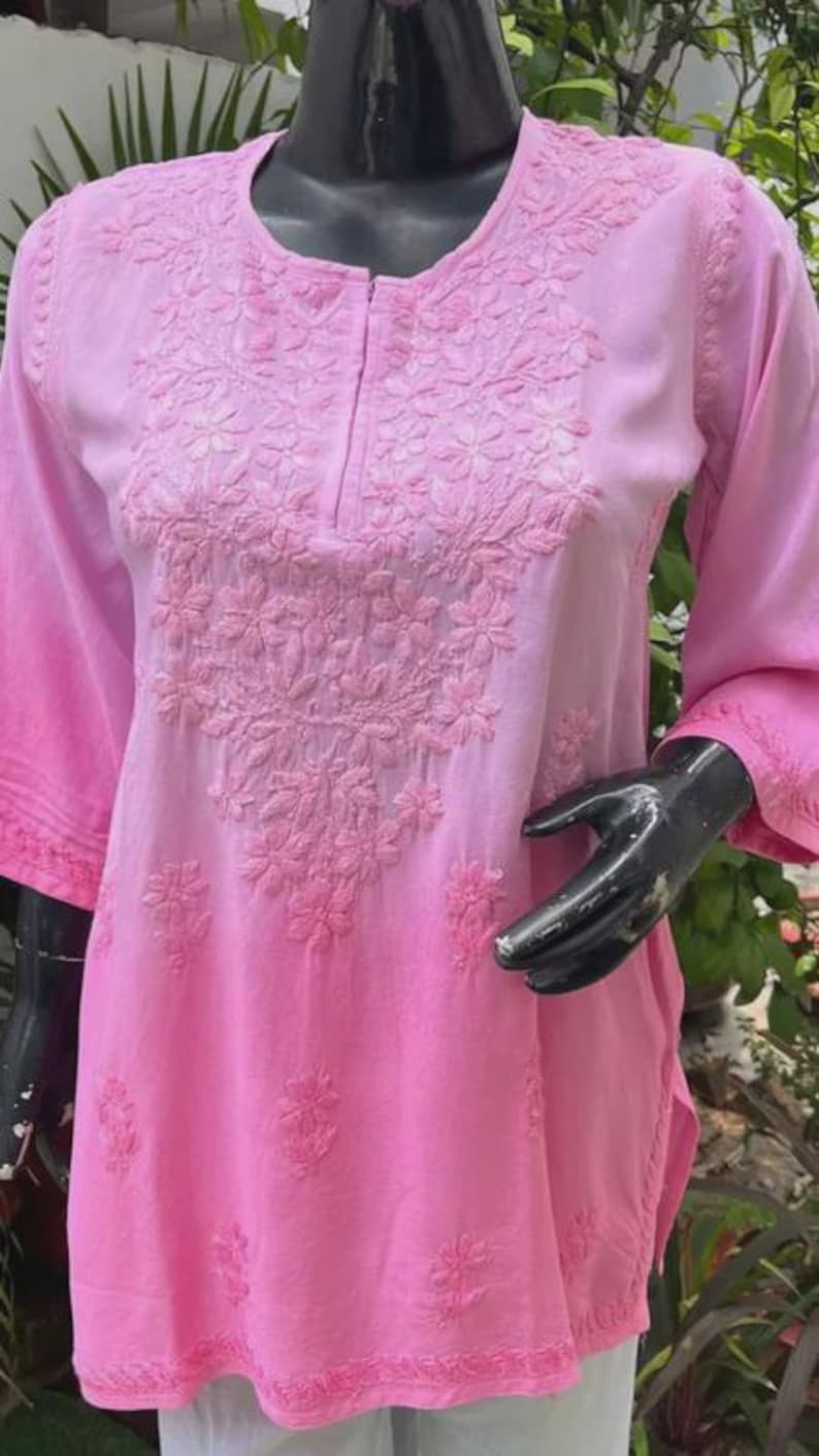 Puede incluir: Una t&uacute;nica rosa con bordados florales. La parte superior presenta un cuello redondo, mangas tres cuartos y un efecto de color degradado de rosa claro a oscuro. El bordado se concentra en el &aacute;rea del pecho.