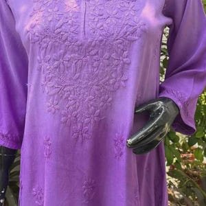 Puede incluir: Una t&uacute;nica lavanda de manga larga con intrincados bordados florales alrededor del cuello y el corpi&ntilde;o. La t&uacute;nica tiene cuello redondo y mangas tres cuartos. La tela parece suave y ligera, adecuada para climas c&aacute;lidos. Se muestra en un maniqu&iacute;.