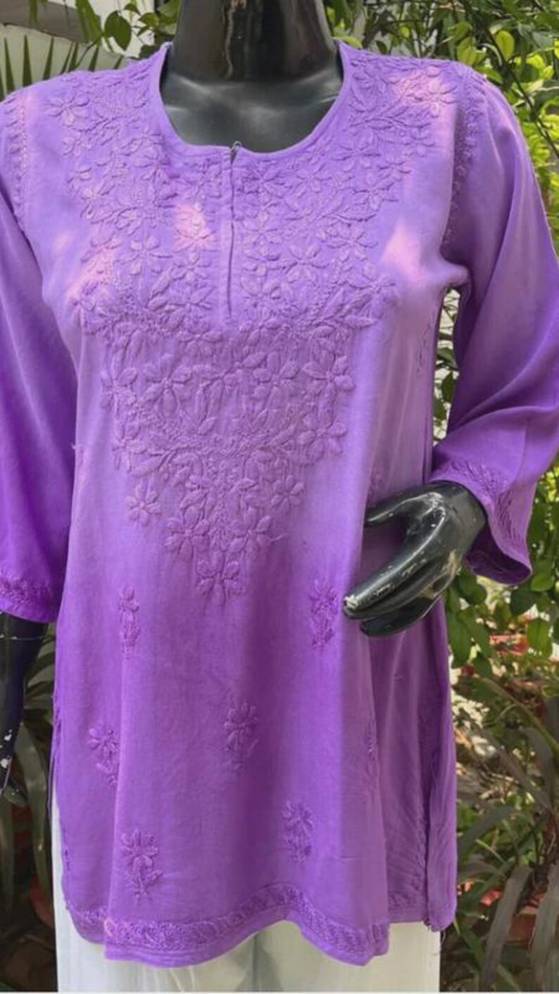 Puede incluir: Una t&uacute;nica lavanda de manga larga con intrincados bordados florales alrededor del cuello y el corpi&ntilde;o. La t&uacute;nica tiene cuello redondo y mangas tres cuartos. La tela parece suave y ligera, adecuada para climas c&aacute;lidos. Se muestra en un maniqu&iacute;.