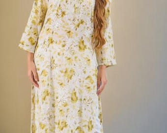 May include: A long-sleeved, knee-length tunic featuring a white base with an olive green floral print and intricate white embroidery around the neckline. The tunic is paired with white cropped trousers that have a detailed embroidered hem.