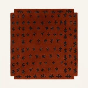 May include: A square rug in a deep terracotta orange color featuring a repeating pattern of small, black, hand-drawn style plant or leaf motifs arranged in a grid. The rug has notched corners, creating a distinct geometric silhouette.