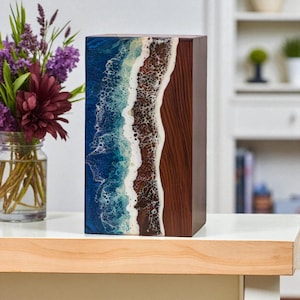 May include: A rectangular wooden box with a unique design. One side features a blue and white ocean wave pattern, while the other side is a rich brown wood grain. The box is displayed on a white surface.