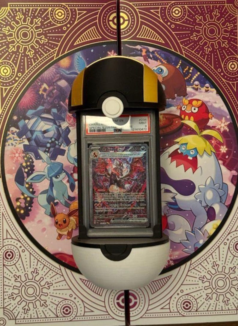 Op de afbeelding: Een zwart, wit en goudkleurig display in de vorm van een Pok&eacute; Ball, met een beoordeelde ruilkaart. De kaart bevat een kleurrijke illustratie van een personage. De achtergrond is een decoratief paneel met Pok&eacute;mon-personages.