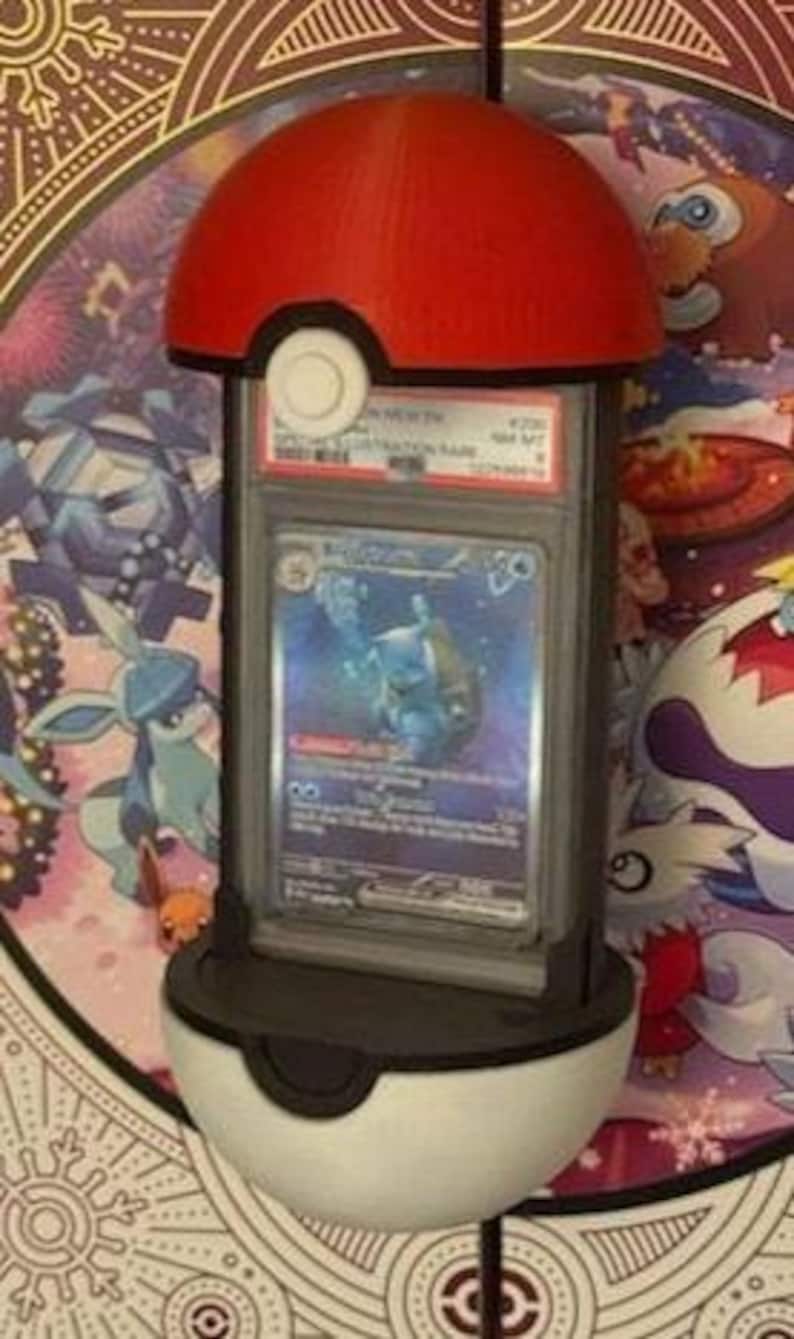 Pode incluir: Um suporte de exibi&ccedil;&atilde;o de Pok&eacute; Bola vermelho e branco segurando uma carta colecion&aacute;vel Pok&eacute;mon classificada. O suporte &eacute; projetado para se assemelhar a uma Pok&eacute; Bola, com um topo vermelho e uma parte inferior branca. O cart&atilde;o est&aacute; em um suporte de prote&ccedil;&atilde;o.