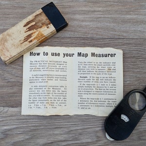 Könnte beinhalten: Ein schwarz-weißes Anleitungsblatt für einen Kartenmesser mit einer Lupe und einer Meilen-Kilometer-Umrechnungstabelle. Der Text lautet "So verwenden Sie Ihren Kartenmesser".