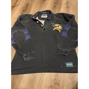 May include: A black long-sleeve shirt with a collar and three buttons. The shirt features a yellow and purple logo on the chest and purple patches on the elbows. The shirt has the word "Throwbacks" on a green tag.