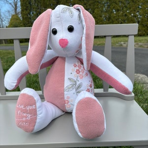 May include: A pink and white bunny rabbit plush toy with embroidered flowers and the words "Love you, Mommy" on the bottom of one foot.