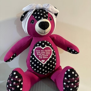 May include: A pink and black polka dot teddy bear with a white headband. The bear has a heart-shaped patch on its chest with the text "Once my clothes now your bear. Hold me close and know I'm there." The bear's paws have embroidered dates.