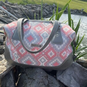May include: A gray and pink patterned tote bag with leather accents and a zipper closure. The bag has two top handles and a small leather tag with the text "Fancy Farm Journey" on it.