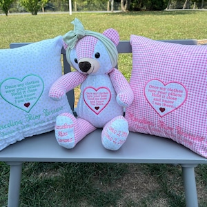 May include: A pink and white gingham teddy bear with a green bow sits between two pillows. The pillows are also pink and white gingham and have embroidered hearts with the text "Once my clothes now your pillow. Hold it close and know I am there."  The pillows are personalized with the names "Marcelina Rios Serrano" and "Marcelina Rios Serrano".