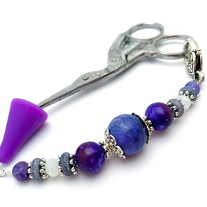 Puede incluir: Encanto de tijeras con cuentas moradas y azules con una punta de silicona morada. El encanto está hecho con una variedad de cuentas, incluyendo amatista, ágata y plata.