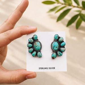 May include: A pair of sterling silver stud earrings featuring clusters of oval-shaped turquoise stones with brown matrix patterns. The earrings are mounted on a white display card with the text STERLING SILVER printed at the bottom.