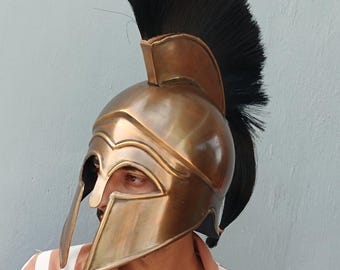 Può includere: Un elmo spartano color bronzo con un pennacchio nero. L'elmo presenta un design curvo con protezioni per le guance e una cresta prominente. Questa replica storica è un simbolo degli antichi guerrieri greci.