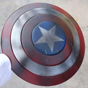 May include: A round shield with a red, silver, and blue color scheme. The shield features concentric circles with a central blue circle containing a silver five-pointed star. The outer ring is red, with silver and black accents.