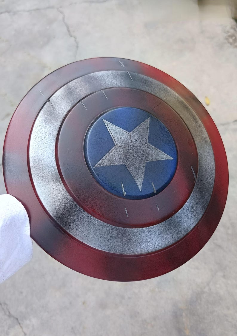 May include: A round shield with a red, silver, and blue color scheme. The shield features concentric circles with a central blue circle containing a silver five-pointed star. The outer ring is red, with silver and black accents.