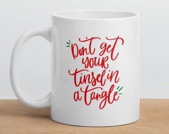 May include: White ceramic mug with a red and green design. The mug has a handle and says "Don't get your tinsel in a tangle".