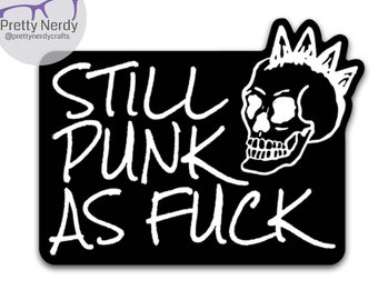 May include: A rectangular black sticker featuring white hand-lettered text that reads STILL PUNK AS FUCK. To the right of the text is a white graphic illustration of a human skull with a mohawk hairstyle, all set against a plain white background.