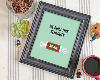May include: A framed print with a light green background and the text "We built this schmidty All day". The print is in a black frame and is sitting on a white and gray striped surface.