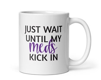 May include: White ceramic coffee mug with black text that reads "Just wait until my meds kick in". The word "meds" is in purple.