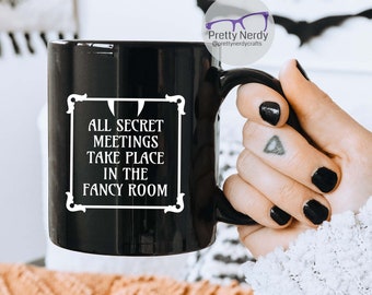 May include: Black coffee mug with white text that reads "All secret meetings take place in the fancy room".