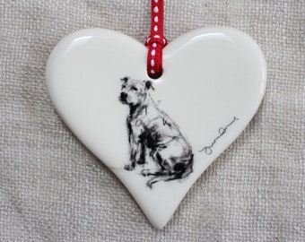 May include: A heart-shaped ceramic ornament with a black and white illustration of a dog. The ornament has a red and white polka dot ribbon for hanging. The dog is sitting, and the ornament has a glossy finish.
