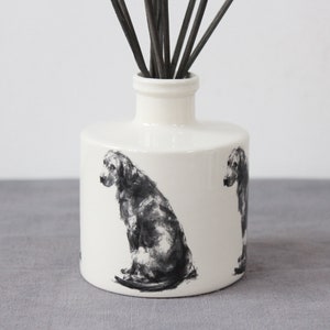 May include: White ceramic diffuser bottle with a black and white illustration of a dog on each side. The bottle has a black lid and is filled with black diffuser sticks.
