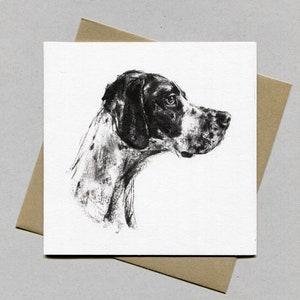 Peut inclure: Carte carrée avec un dessin au fusain du profil d'un chien. Le chien a un pelage noir et blanc et regarde sur le côté. La carte est posée sur une enveloppe marron, créant une présentation simple et élégante.