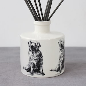 Peut inclure: Diffuseur en céramique blanche avec une illustration en noir et blanc d'un golden retriever sur chaque côté. Le flacon est muni de bâtonnets diffuseurs noirs.