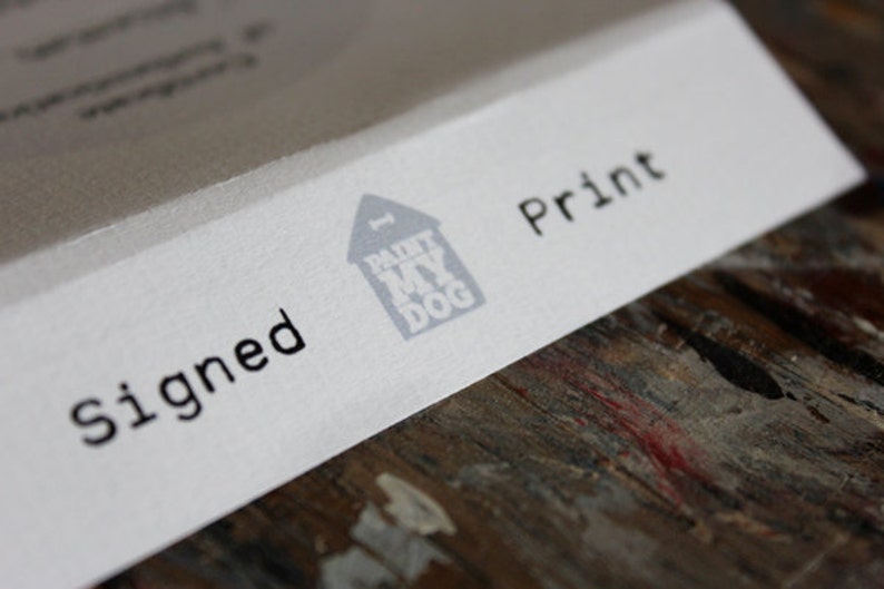 Op de afbeelding: Een witte kaart met de woorden "Gesigneerd" en "Print" in zwarte tekst. Een grijs huis met een hondenbot erbovenop en de woorden "Paint My Dog" erin, bevindt zich in het midden van de kaart.