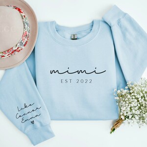 May include: Light blue sweatshirt with the text "mimi est 2022" on the front and the names "Luke, Connor, Emma" with a heart on the left sleeve.