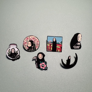 May include: A selection of six enamel pins featuring the character No-Face from the animated film Spirited Away. The pins depict No-Face in different scenes, including a jar, a floral design, and a Japanese landscape. One pin reads "BUT FIRST COFFEE."